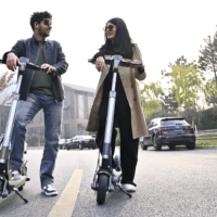 Two riders on TK2 electric scooters in a parking lot