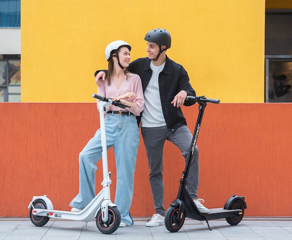 Two riders with scooters against a yellow wall